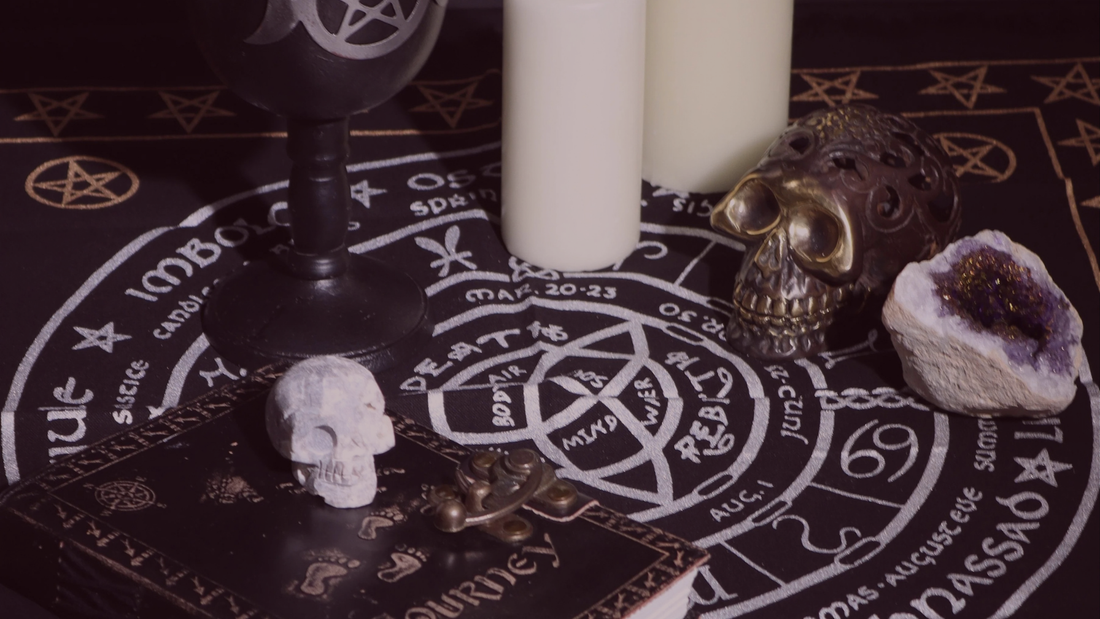 Samhain altar showing skull decorations, white candles, a closed grimoire and a wheel of the year altar cloth