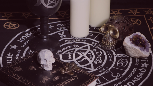 Samhain altar showing skull decorations, white candles, a closed grimoire and a wheel of the year altar cloth
